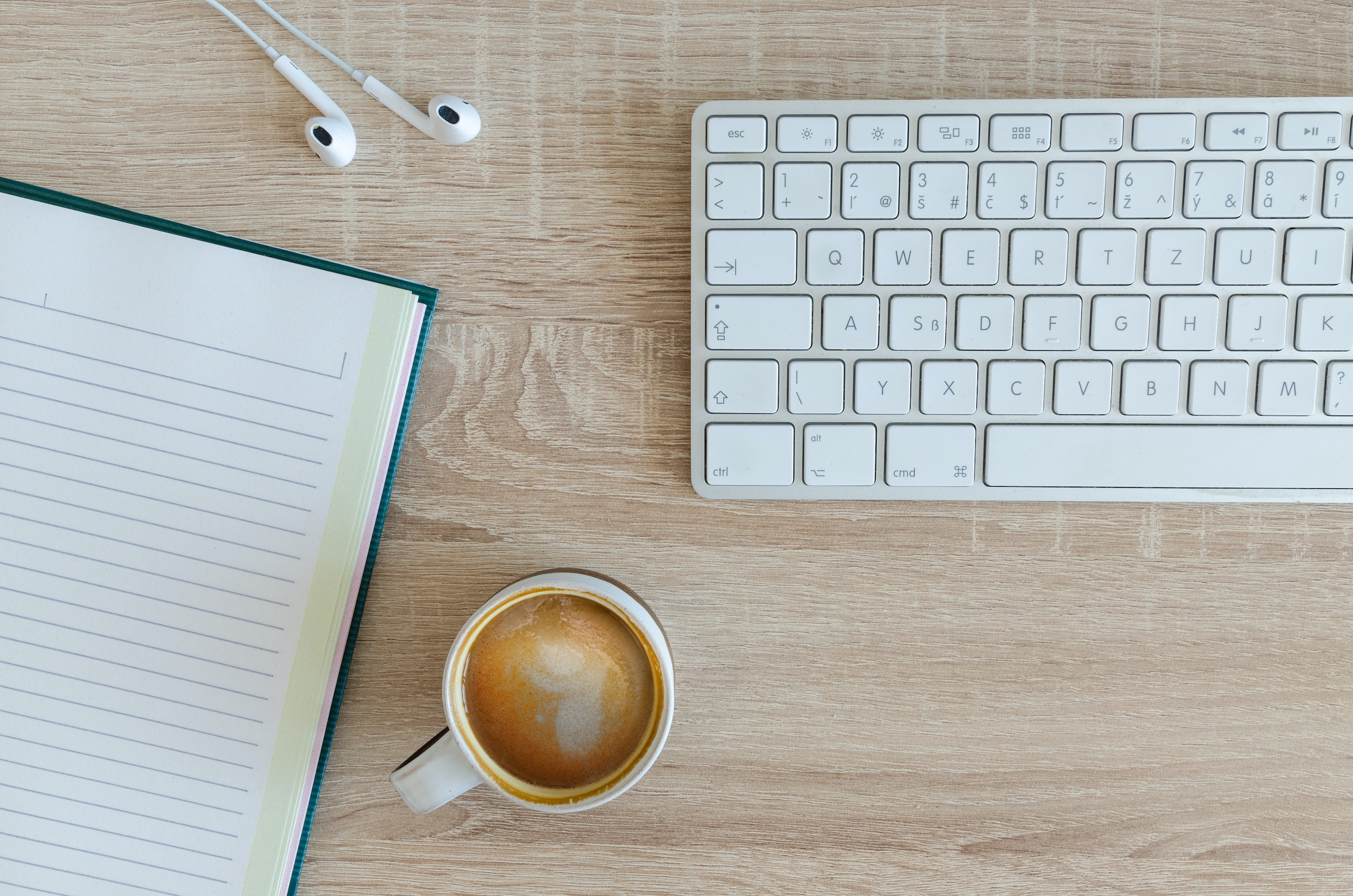 Escritorio con una libreta, un café y un teclado de ordenador