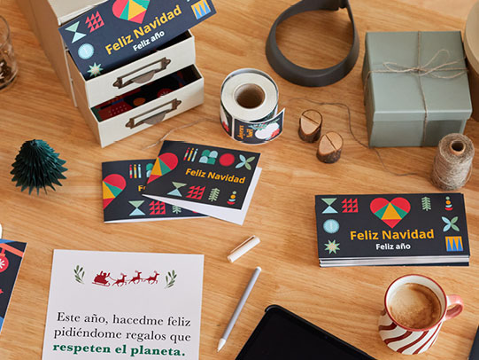 Mesa de escritorio con postales de navidad, etiquetas navideñas y una taza de café